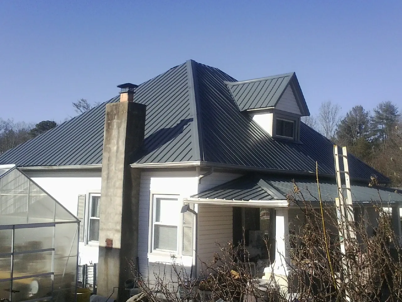 Dark blue standing seam metal roof on a white farmhouse with dormer — Slate & Tile Roof Repair by Roofing Brothers in Salida