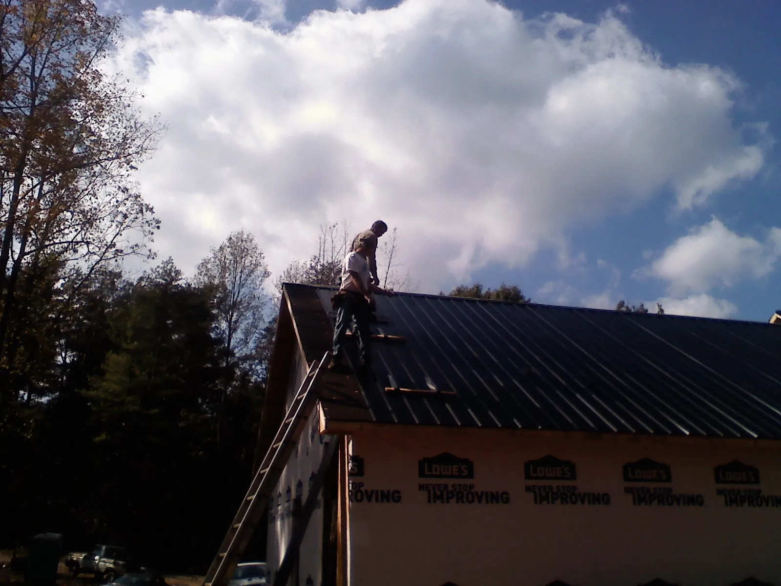 Roofer fastening dark metal panels high against a cloudy sky, from a Roof Inspection job in Salida