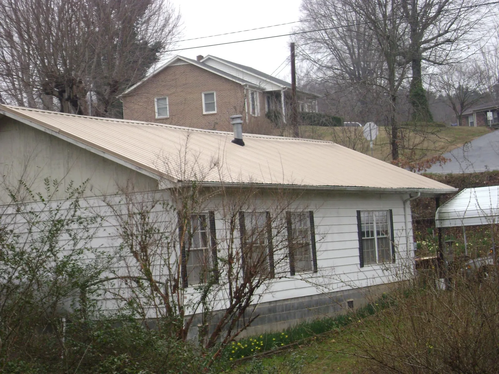 Tan metal roof on a white sided house set into a hillside — Commercial Roofing by Roofing Brothers in Salida